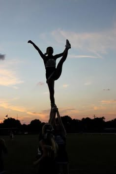 a cheerleader is standing on top of another cheerleader in the air at sunset