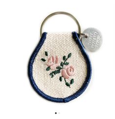 an embroidered keychain with pink flowers on it and a blue ribbon around the edge