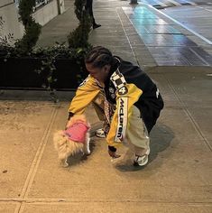 a woman bending over to pet a small dog on the sidewalk in front of a building