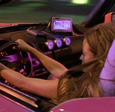 a woman sitting in a pink car with her hands on the steering wheel