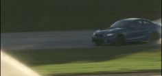 a blue car driving down a race track next to a green grass covered field and water spout