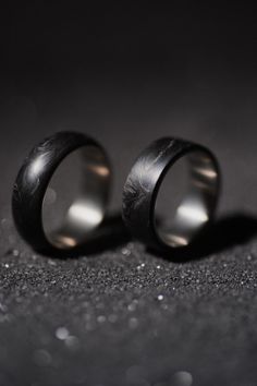 two wedding rings sitting next to each other on top of a black cloth covered floor