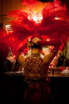 a woman in a red dress is holding a large feathered object up to her head