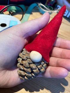 a hand holding a small pine cone with a santa hat on it