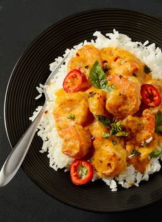 a black plate topped with rice and shrimp next to a silver serving fork on top of it