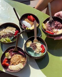 four bowls filled with different types of food on top of a green table next to a person's hand