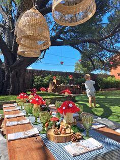 an outdoor table set up for a party with red flowers and mushrooms hanging from the ceiling