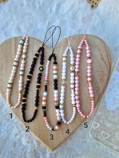 six beaded necklaces are arranged on a heart - shaped wooden board with numbers