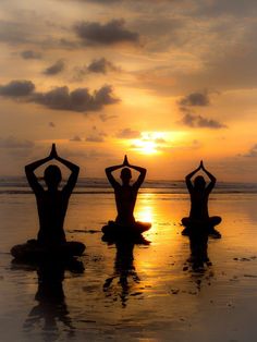 three people sitting on the beach doing yoga exercises at sunset with their hands in the air