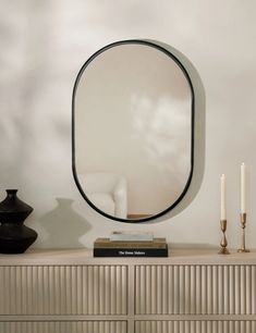 a mirror sitting on top of a dresser next to a white chair and two candles