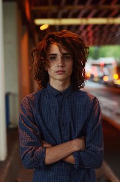 a young man with his arms crossed standing in front of a train platform at night