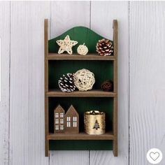 a wooden shelf with christmas decorations on top and pine cones in the bottom, sitting against a white painted wall