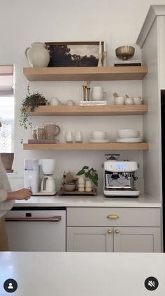 a woman standing in front of a kitchen counter filled with white dishes and coffee cups