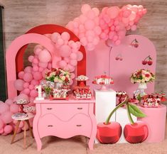 a pink table topped with lots of desserts and balloons in front of a wall