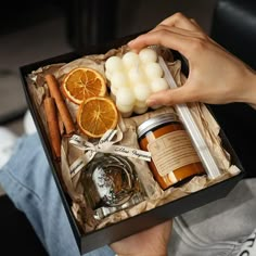 a person holding an open box filled with oranges, cinnamon sticks and other items