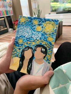 a person holding up a piece of art that looks like the starry night with two people