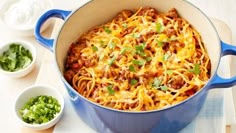 a blue pot filled with spaghetti and topped with green onions, cheese and cilantro