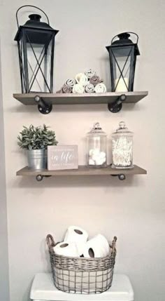 two shelves above a toilet with towels and baskets on top of them, along with candles