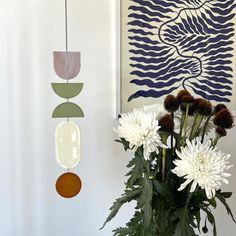 a vase filled with white flowers sitting next to a wall mounted art piece on the wall