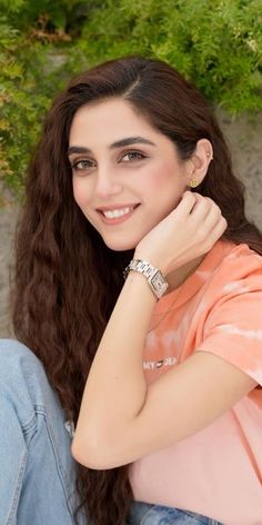 a young woman sitting on the ground with her arm around her neck and smiling at the camera