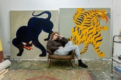 a woman sitting in a chair next to two paintings on the wall and one with a tiger