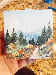 a hand holding up a small card with trees in the background and mountains in the distance