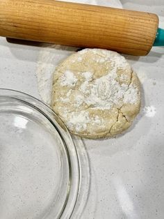 an uncooked dough and rolling pin on a white counter top next to a glass bowl with powdered sugar