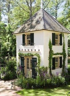 a white house with green shutters and ivy growing on the roof, surrounded by greenery