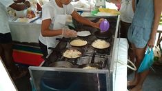 two women preparing food on top of an oven in a kitchen with other people standing around