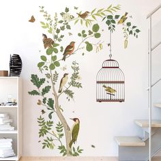 a birdcage hanging on the side of a wall next to a tree with birds in it