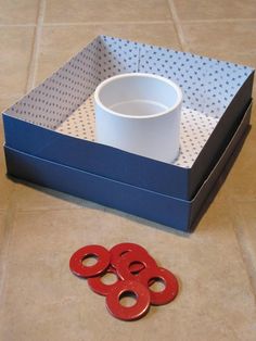 a blue box with three red circles on the floor next to it is a white cup and four red rings