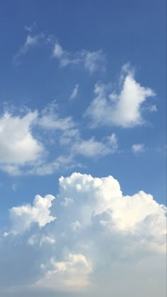 a plane flying high in the sky with white clouds behind it and blue skies above