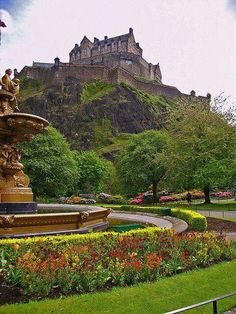 a fountain in the middle of a garden with a castle in the background