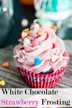 a cupcake with pink frosting and sprinkles is on a wooden table