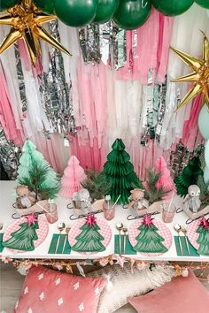 a table topped with lots of green and pink christmas tree decorations next to giant balloons