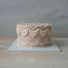 a pink cake sitting on top of a white plate covered in icing and lace