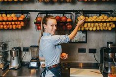 a woman is standing in front of a counter with oranges and apples on it