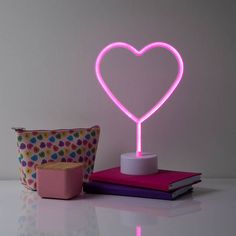 a pink heart shaped neon light sitting on top of a table next to a cup