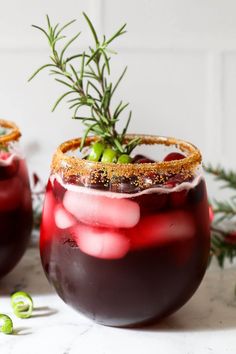 two glasses filled with red wine and garnished with sprigs, on a white surface