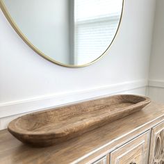 a large wooden bowl sitting on top of a dresser next to a wall mounted mirror