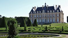 a large building with lots of hedges in front of it and a pond surrounded by trees