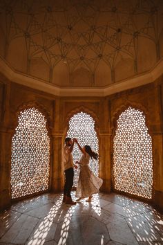 a man and woman dancing in an ornate room with arched windows on either side of them