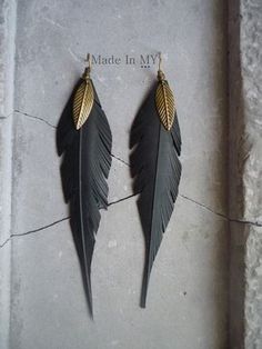 two pairs of black feathers with gold leaves hanging from them on a stone slab that says made in my