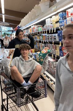 two boys are sitting in a shopping cart at the grocery store and one boy is holding food