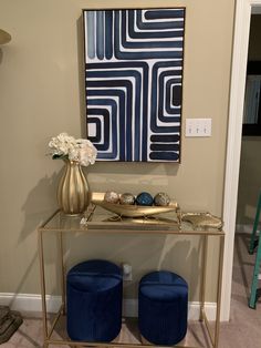 a blue and gold console table with two stools in front of it on carpeted floor