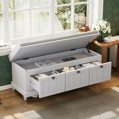 a white storage bench with drawers in front of a window and table next to it