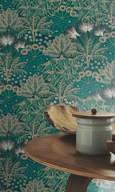 a wooden table topped with a bowl filled with fruit next to a green wallpaper