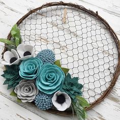 a wreath made out of paper flowers sitting on top of a white wooden table next to a wire fence