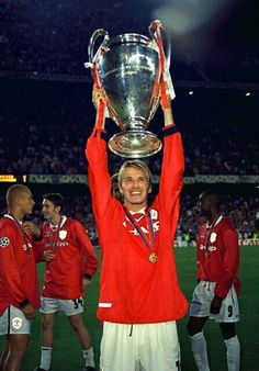 a man holding up a trophy in front of his face on a soccer field at night