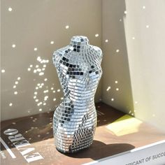 a shiny silver sculpture sitting on top of a book shelf next to a window sill